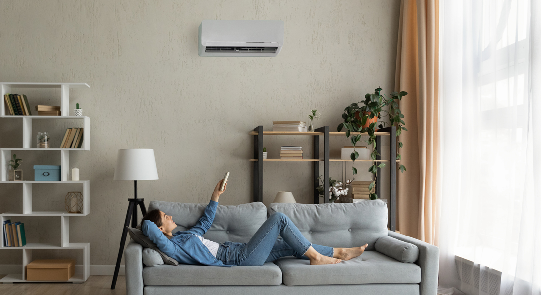 rapariga deitada no sofá a ligar o ar condicionado com inverter com comando